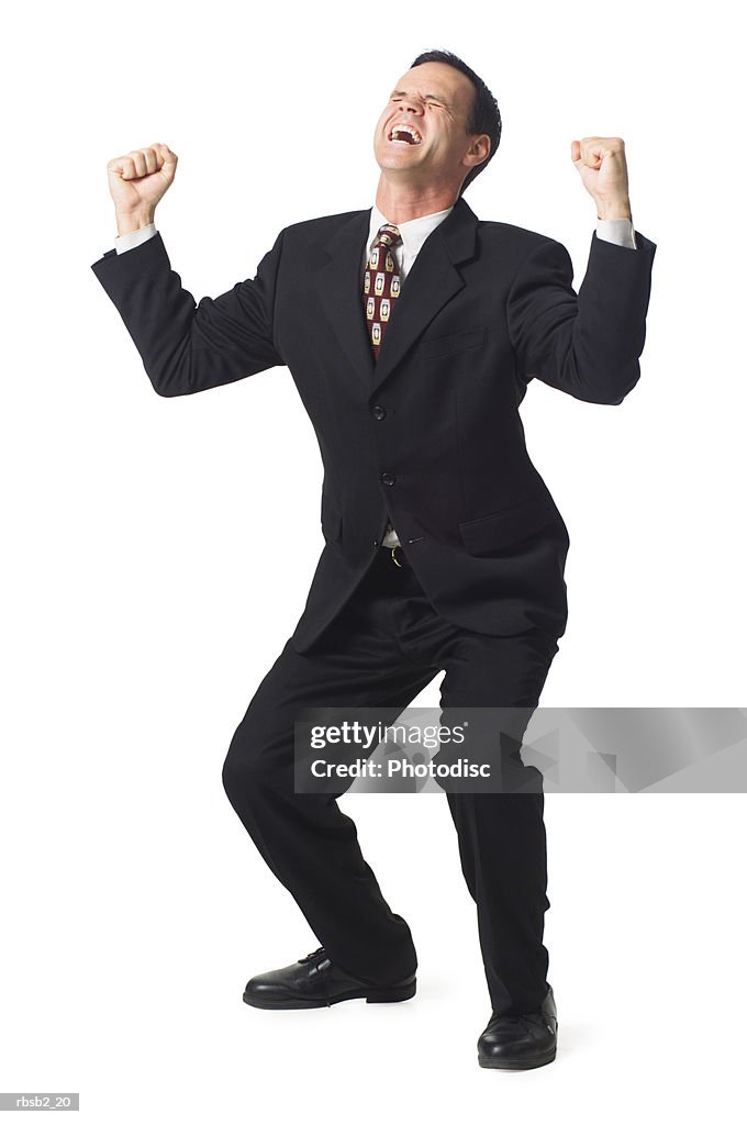 A caucasian business man in a dark suit holds up his arms in celebration