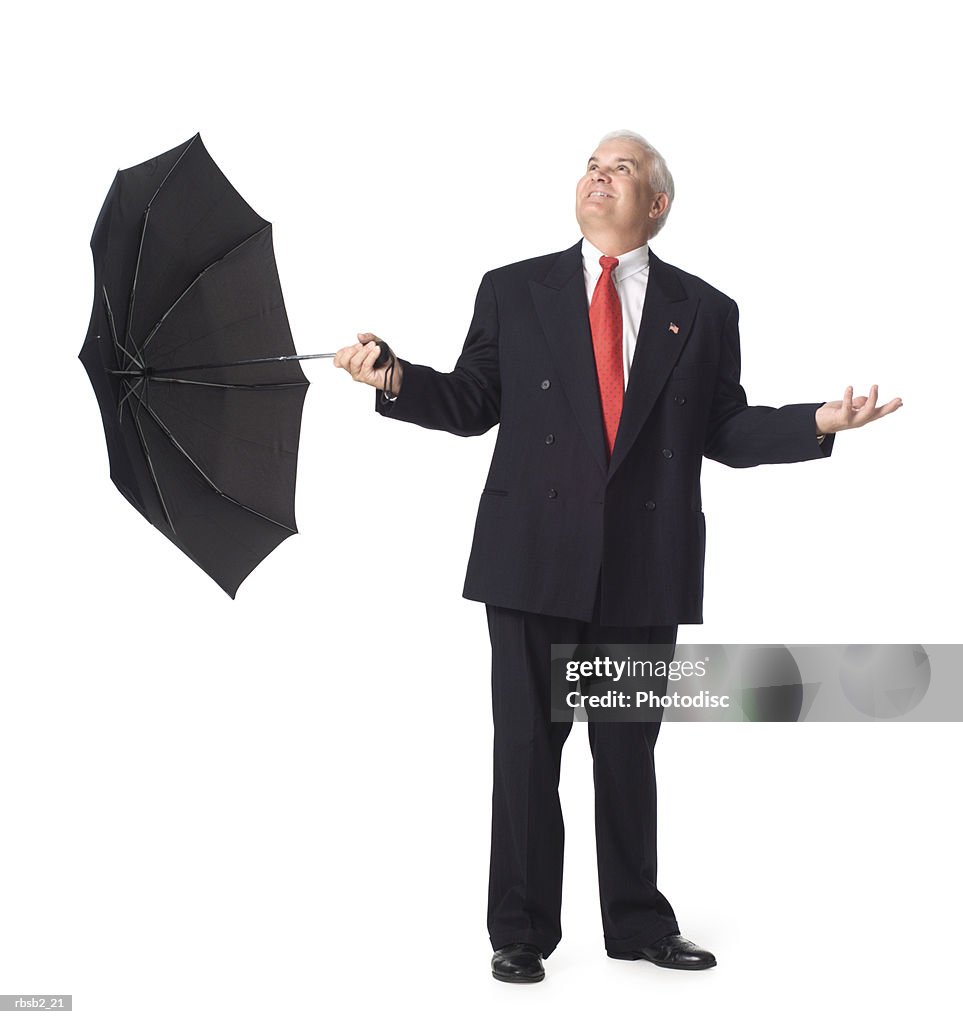 A caucasian business man in a dark suit holds an umbrella and looks upward