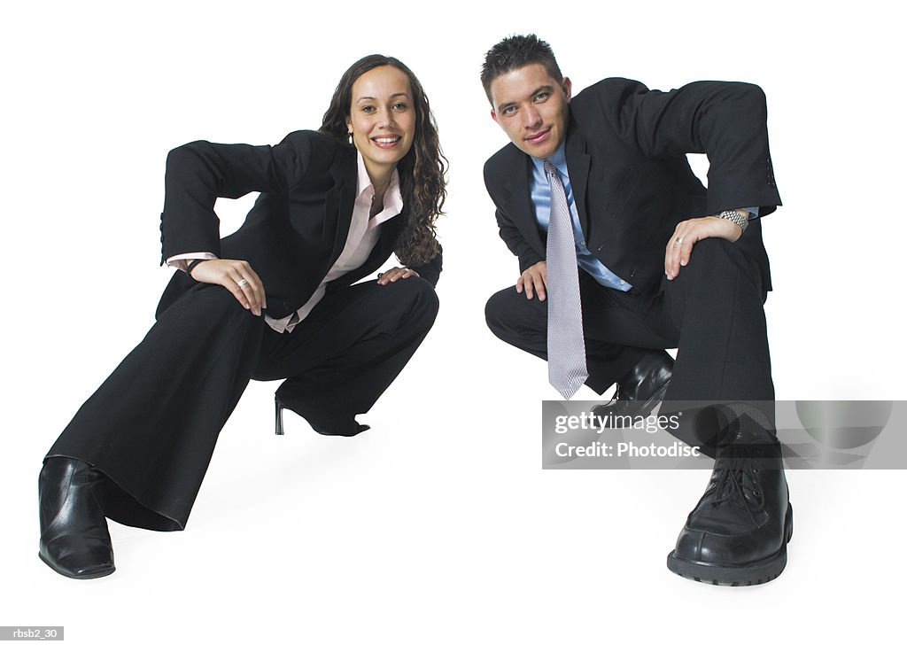 Two ethnic business people crouch down in a fun action pose and smile