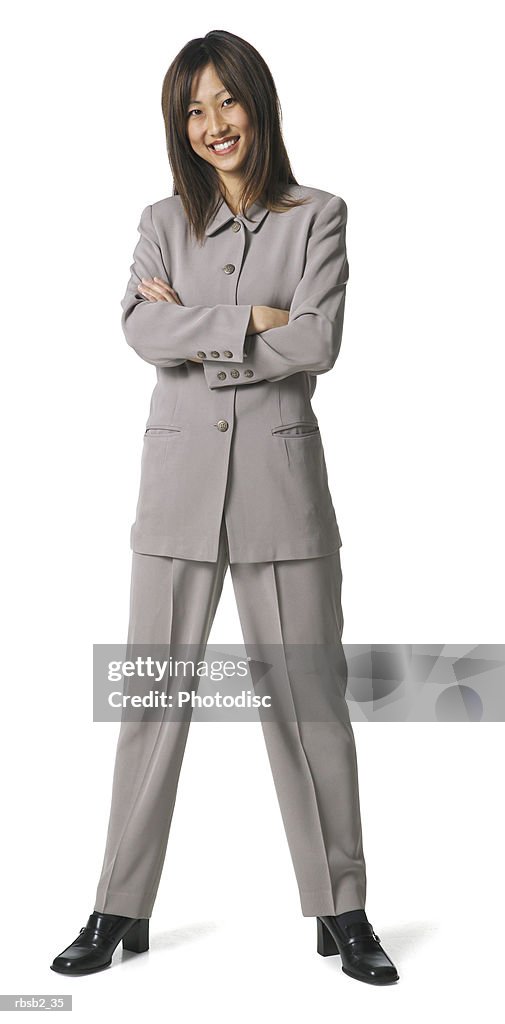 An asian business woman in a grey pant suit folds her arms and smiles