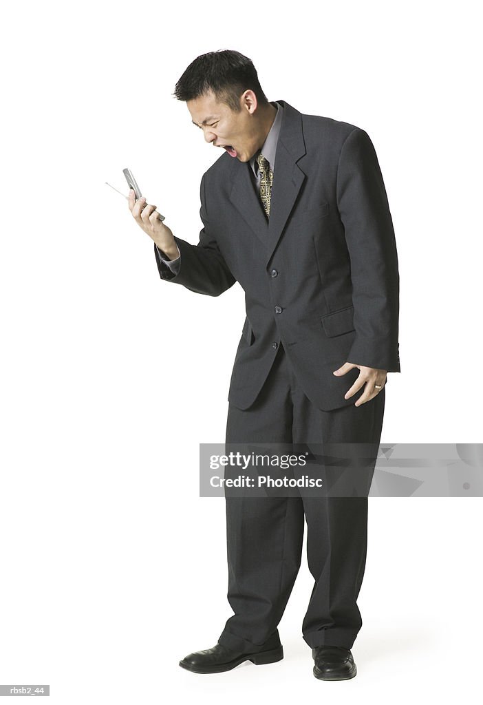 An adult asian business man in a dark suit yells angrily into his cell phone