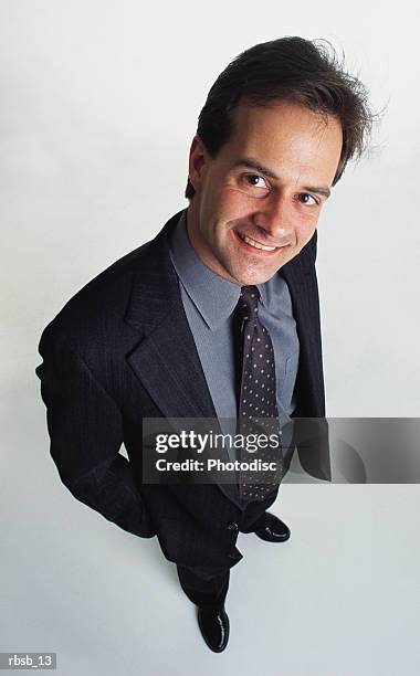 handsome caucasian dark haired male in a dark suit with a blue shirt and tie stands smiling into the camera - male portrait suit and tie stock-fotos und bilder