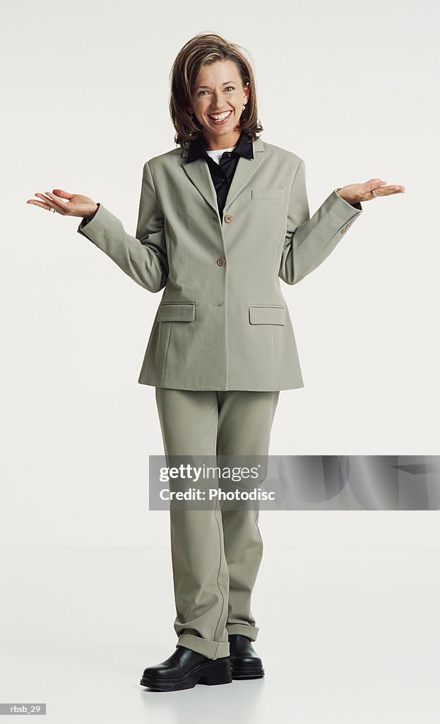 An attractive young caucasian woman with blue eyes and shoulder length brown hair in a green shirt and and grey pants stands looking into the camera with her hands up in a shrugging gesture