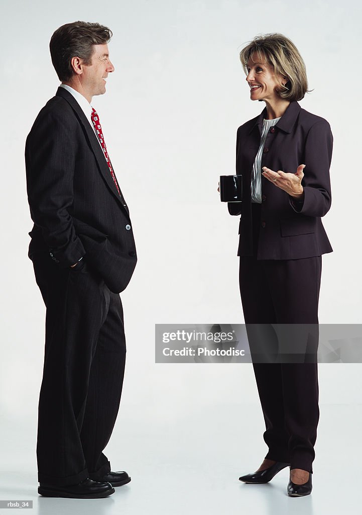 A handsome middle aged caucasian business man and an attractive middle aged business woman in dark business suits are conversing with eachother