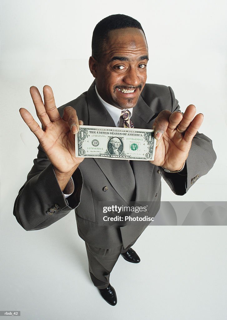 A handsome young african american man in grey business suit is presenting a dollar bill to the camera