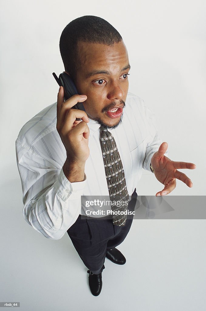 A handsome young african american man in a white shirt and dark slacks talking into a cell phone