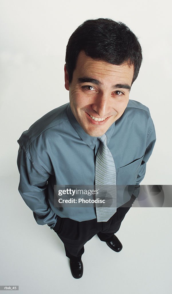 A handsome young caucasian man with short dark hair dressed in a blue shirt and dark slacks is looking up into the camera with a look of confidence