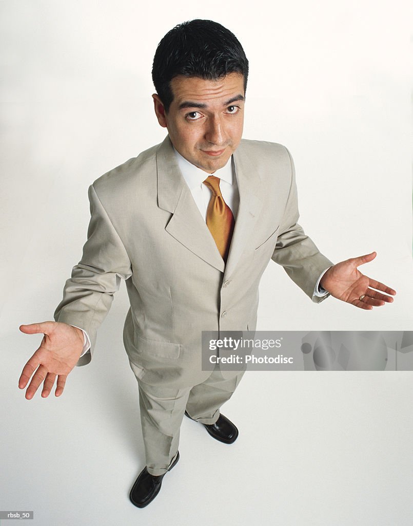 A handsome young ethnic business man  with short dark hair is dressed in a light business suit looking up at the camera with his arms out in a shrugging gesture