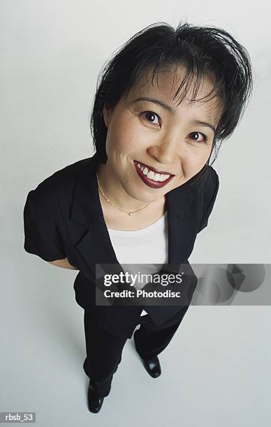 an attractive young asian woman with short dark hair dressed in a dark suit and white shirt is looking up into the camera with her hands behind her back - white shirt ストックフォトと画像