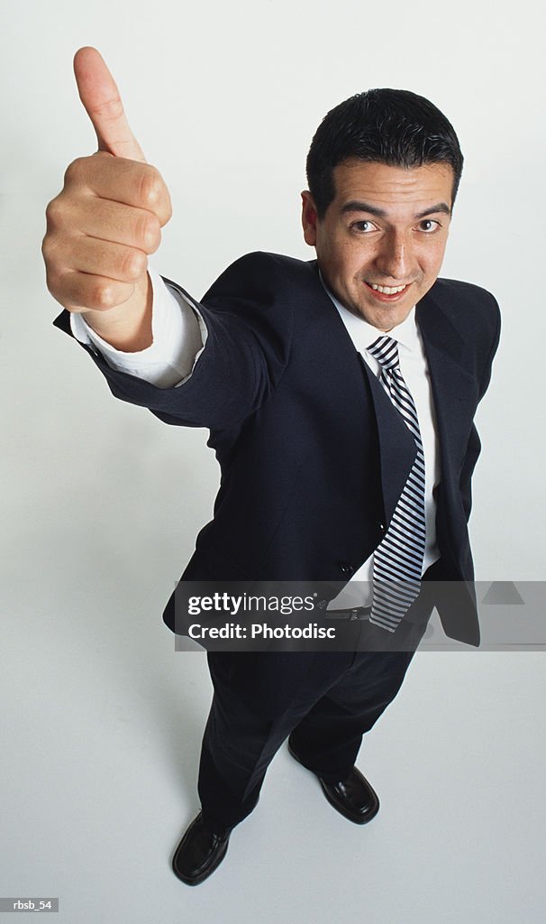 Handsome young ethnic businessman short dark hair in dark blue suit looks to camera gives thumbs up