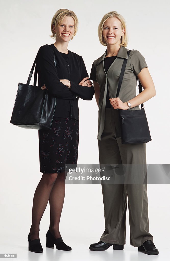 Two beautiful  young caucasian women with shoulder length blond hair dressed in businees attire and purses standing together smiling into the camera