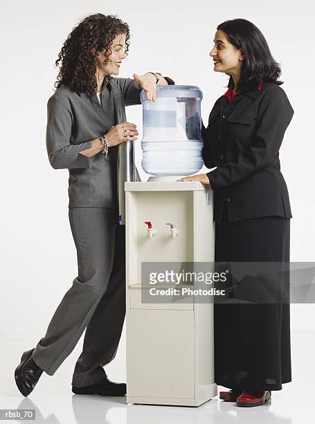 two attractive young women in business attire standing around a water cooler conversing with eachother - water cooler white background stock pictures, royalty-free photos & images