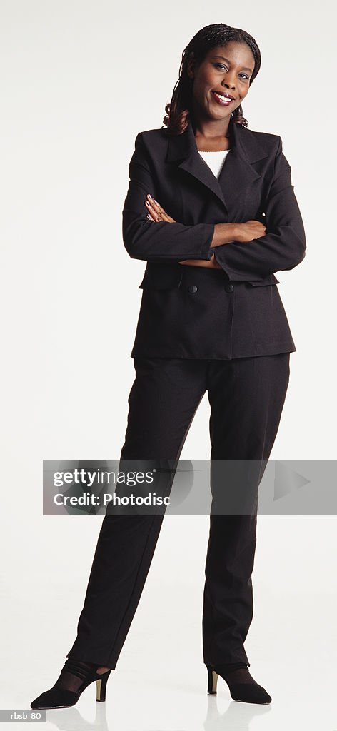 A beautiful young african american woman with long hair dressed in a dark black suit standing looking into the camerawith her arms crossed