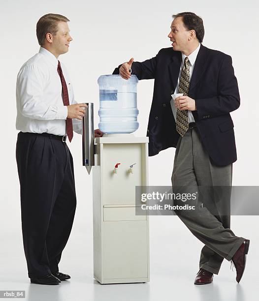 two young caucasian businessmen are standing around a watercooler conversing with eachother - water cooler white background stock pictures, royalty-free photos & images