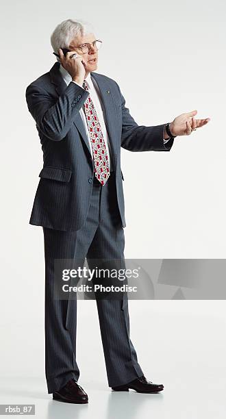 a handsome mature caucasian businessman with glasses and white hair dressed in a grey business suit speaking into a cell phone hand held out in a conversive gesture - male hair hand ストックフォトと画像