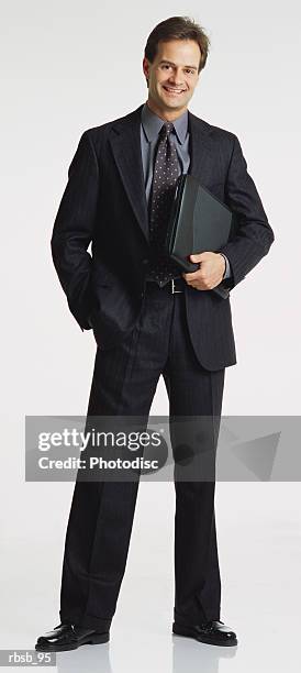 handsome young caucasian businessman in a dark suit facing the camera tucking a laptop under his arm - business person facing away from camera stockfoto's en -beelden