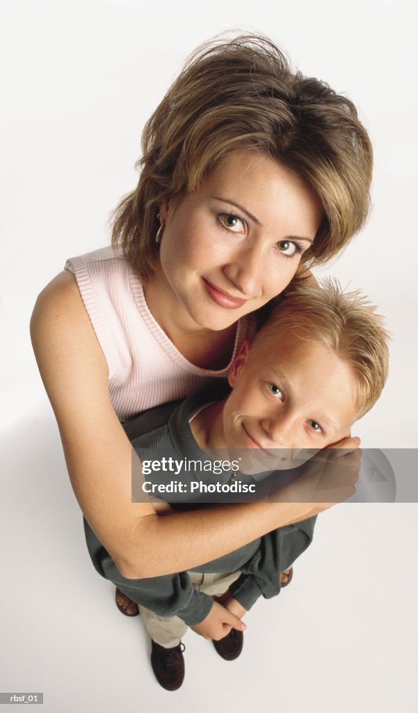 Caucasian woman in pink shirt with brown hair stands with arms around preteen blonde son