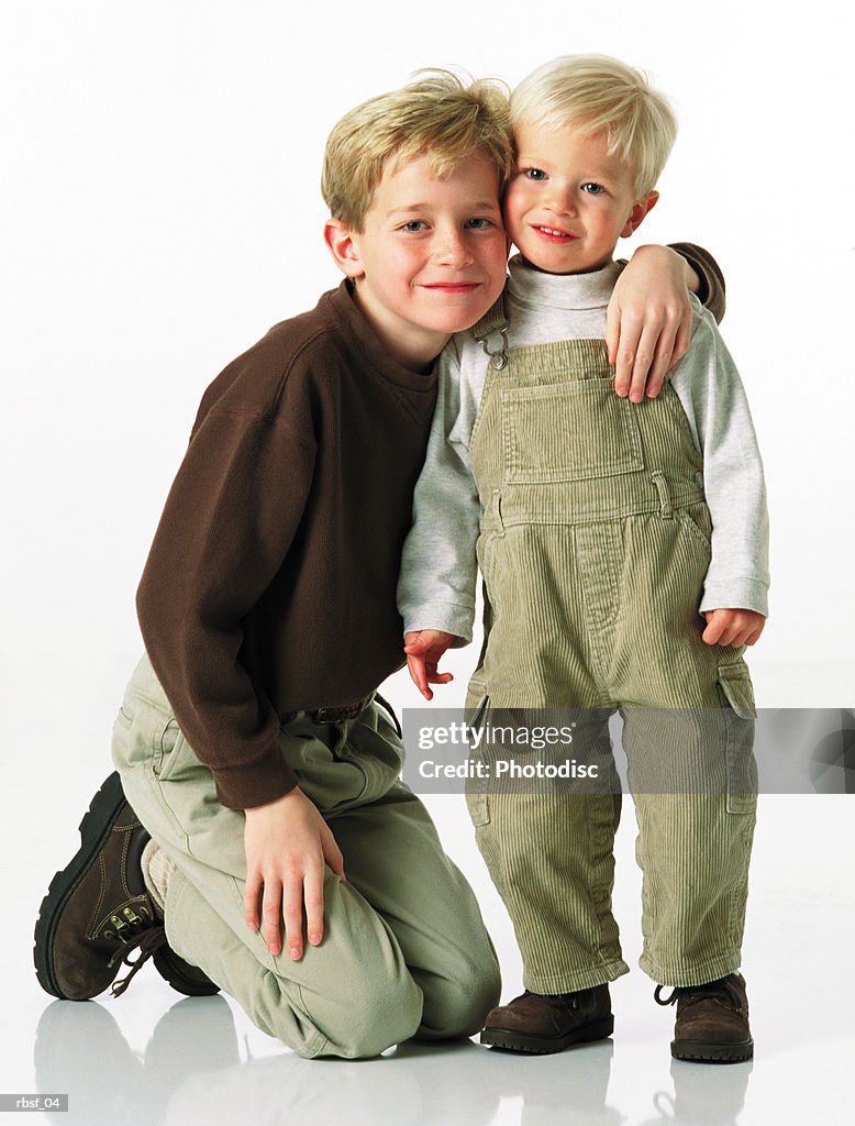 Blonde caucasian boy in khakis on knees with arm around little brother in overalls