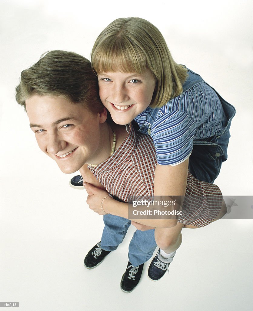 Happy caucasian teenage boy gives his teen sister a piggy-back ride
