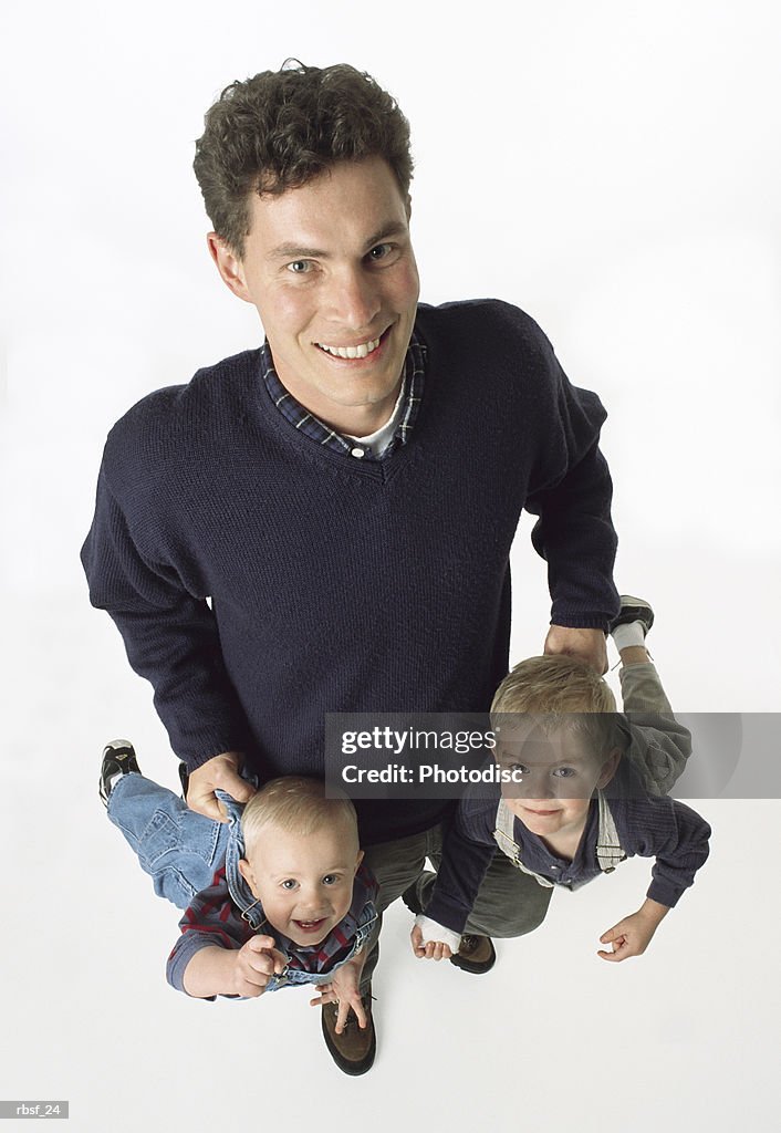 Caucasian brown haired single father holds two young sons by their pants laughing
