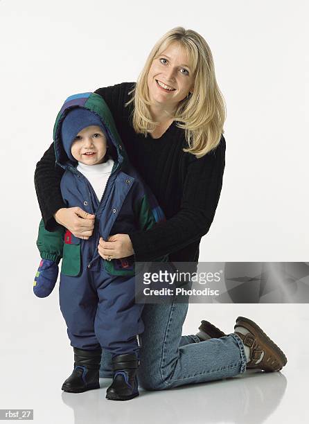 blonde mom kneels behind young son putting his coat on with a smile - smile stockfoto's en -beelden