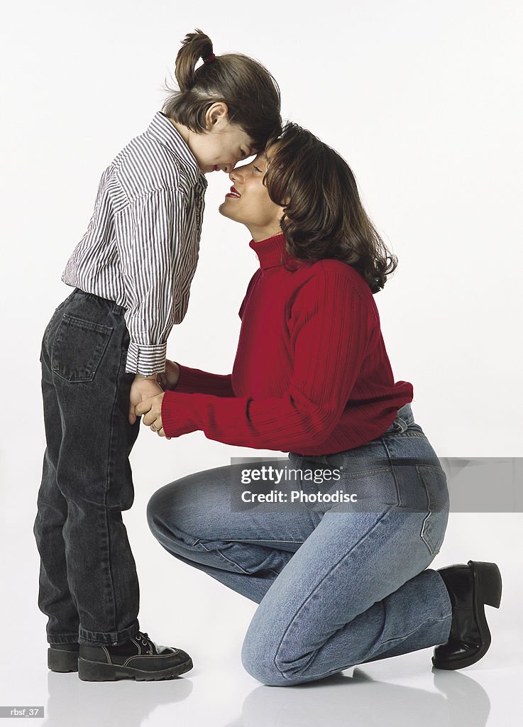 Ethnic mom kneels while holding the hands of young daughter touching nose to nose
