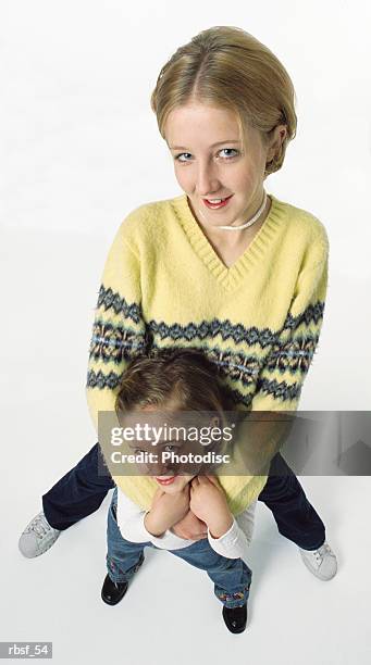 two caucasian blonde sisters stand together with the older sister behind the younger one with arms on her shoulders - breitbeinig stock-fotos und bilder