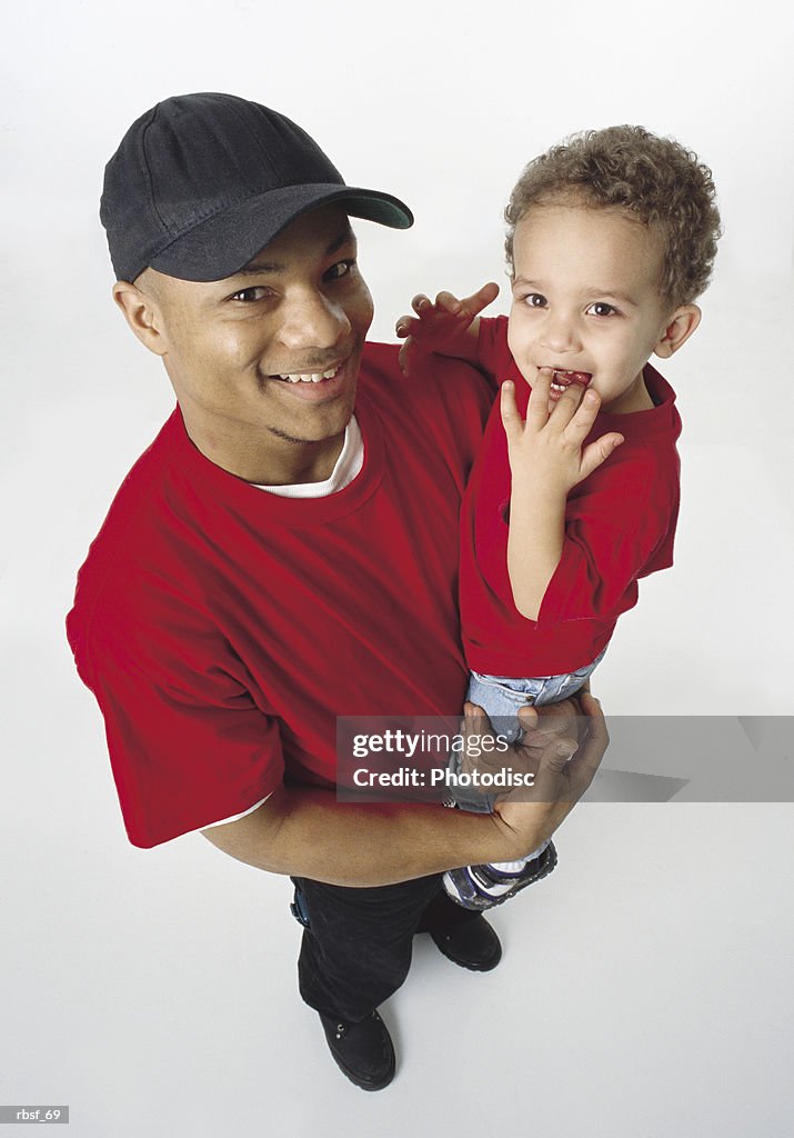 African american single father holds young son and smiles wearing baseball cap and red shirt