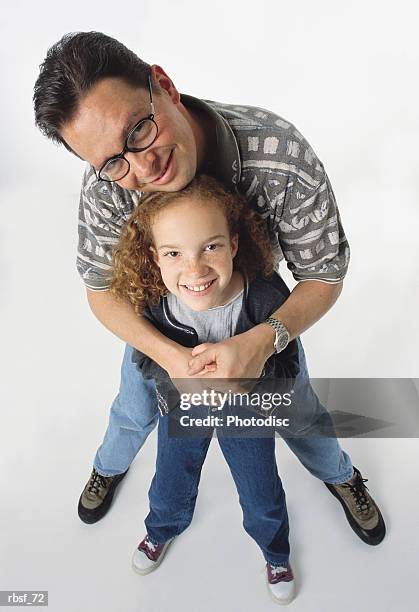 caucasian dad stands behind and holds young redhead daughter who smiles looking up - genderblend stock-fotos und bilder