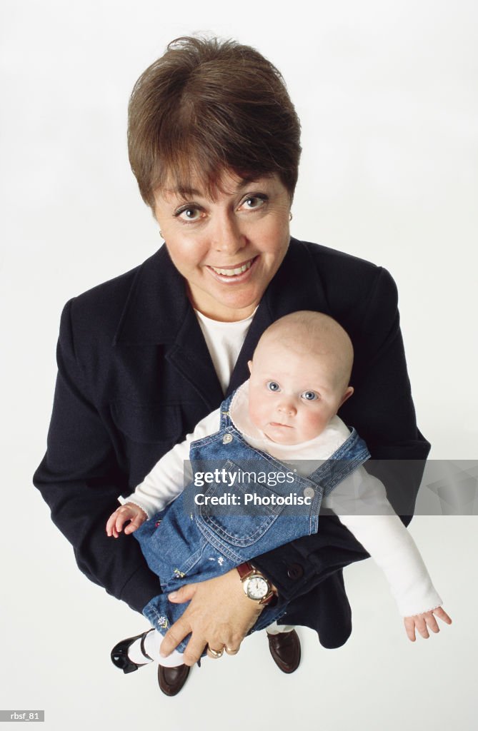 Young caucasian grandmother with short brown hair holds an infant in denim