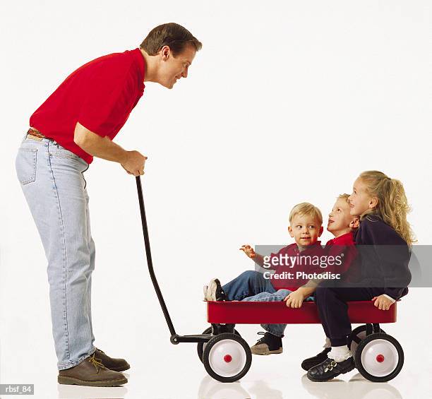 caucasian dad talks to three kids in a red wagon - bollerwagen mann stock-fotos und bilder