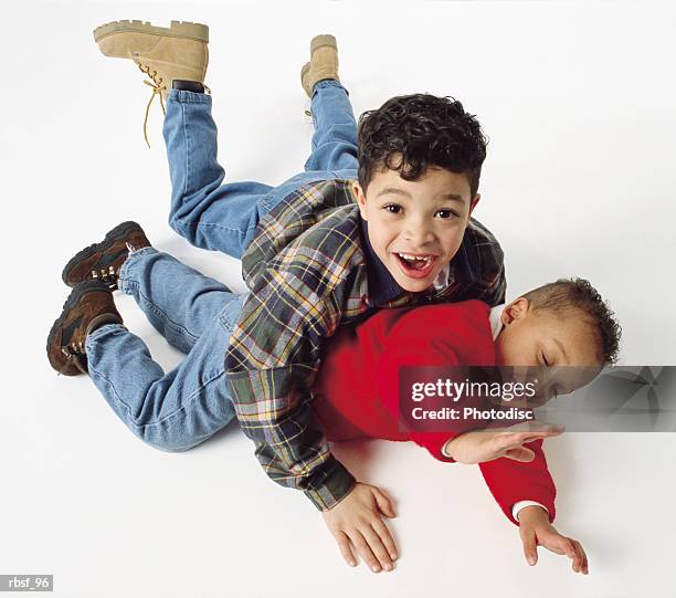 caucasian little boy tackles african american half-brother on floor with both of them laughing - kittle stock-fotos und bilder