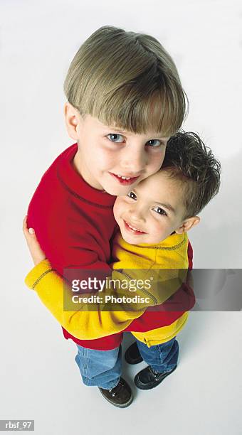 caucasian little brothers hug each other and smile wearing red and yellow shirts - smile stockfoto's en -beelden