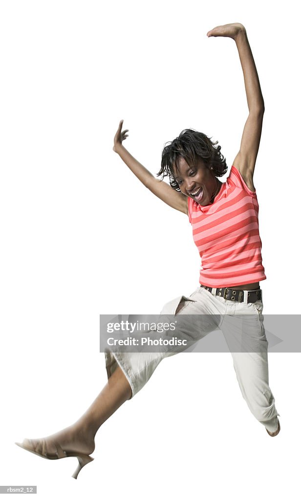 A young adult female in tan pants and a striped shirt puts up her arms and jumps through the air