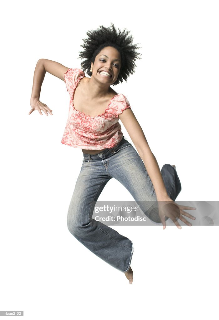 A young adult female in jeans and a floral shirt jumps up playfully