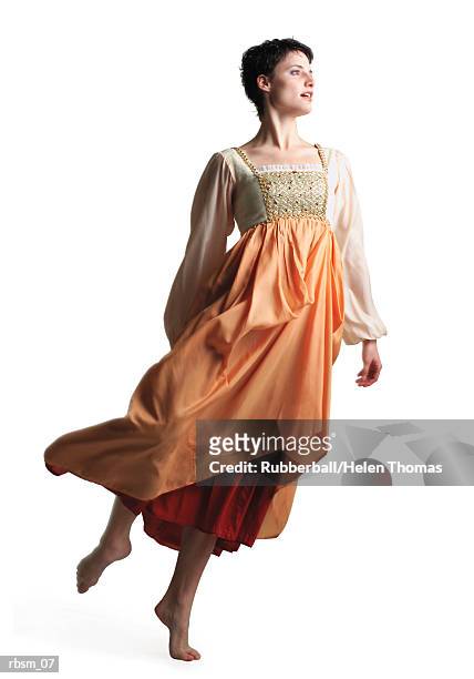 a young caucasian woman in a flowing period costume orange dress lifts herself up on her toe and spins - toe stockfoto's en -beelden