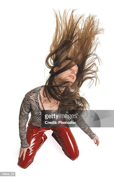 a teenage caucasian girl in red leather pants and a zebra print blouse kneels down and spins she head and makes her hair fly around - down blouse stockfoto's en -beelden