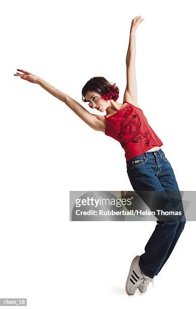 a young caucasian female with black hair with red tips and red tank top jeans and tennis shoes poses leaning to the left with arms in the air - thomas photos et images de collection