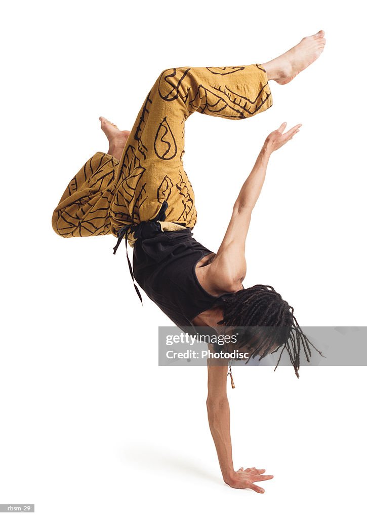 A young african american male modern dancer in yellow pants and a black tank top flips himself upside down with one arm and carefully balances