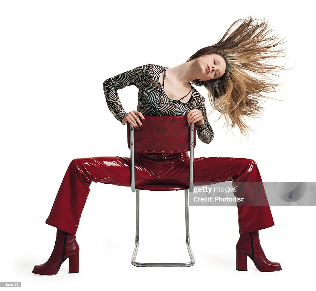 Young female blonde hair in red pants zebra print blouse sits backwards on a chair tosses her hair