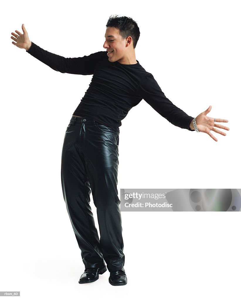A young latin male dancer in black leather pants and a black shirt leans his body back and playfully stretches out his arms as he smiles