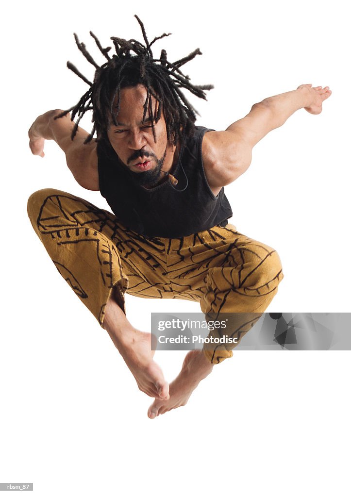 A young african american male modern dancer in gold pants and a black tank top jumps up high and throws his arms back