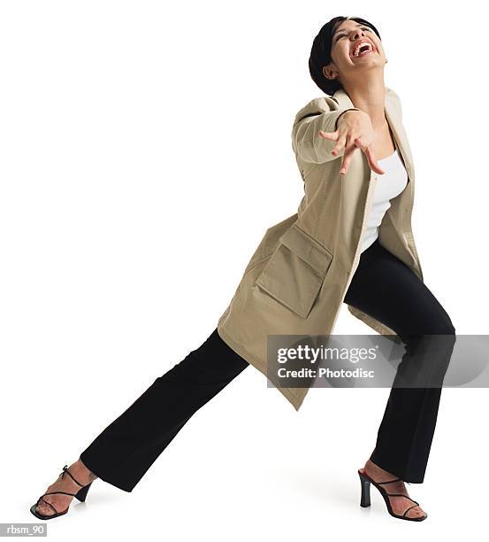 a young attractive latin female in black pants and a tan jacket stretches out her leg and throws one arm forward as she smiles - tan tan stock pictures, royalty-free photos & images