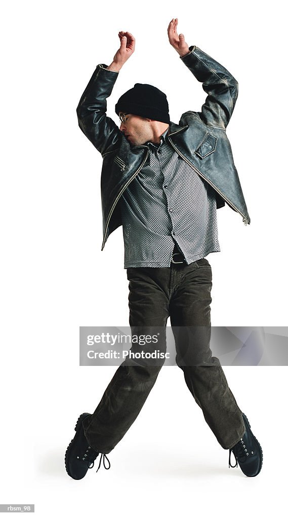 Young male modern dancer in black leather jacket knit cap balances on toes raises his arms overhead