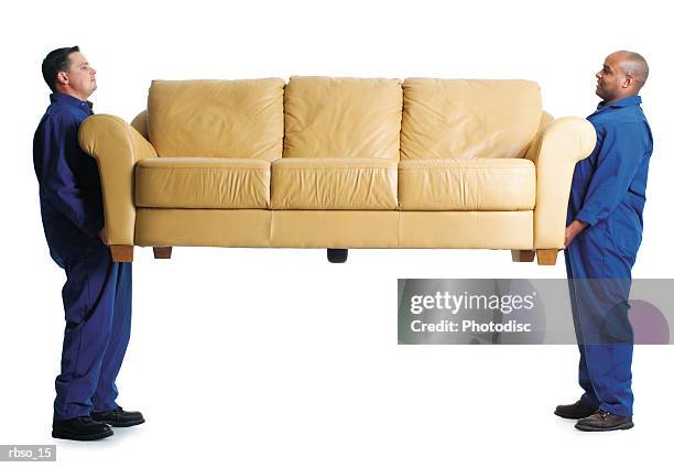 a caucasian male and an african american male mover carry a couch together - removal men imagens e fotografias de stock