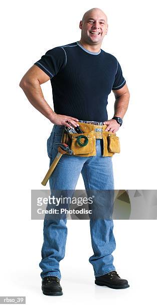 a bald caucasian male builder wearing a tool belt puts his hands on his hips and smiles - belt stockfoto's en -beelden