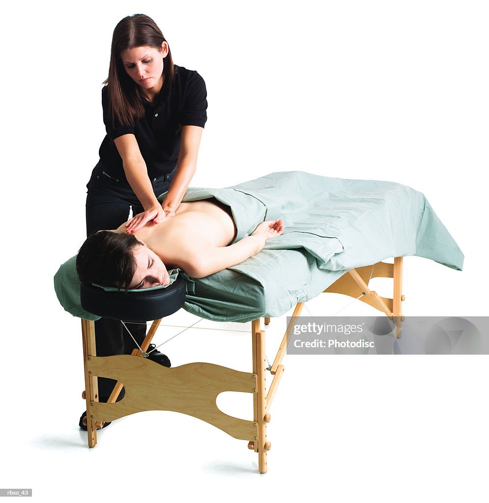 A young caucasian female masseuse massages a woman lying on the table