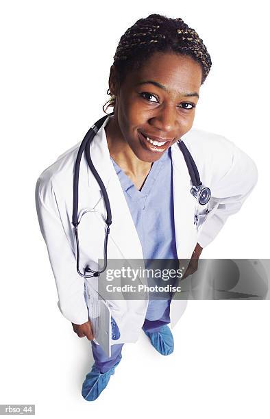 a young african american female doctor in scrubs and a lab coat smiles and looks up at the camera - lab coat stock-fotos und bilder