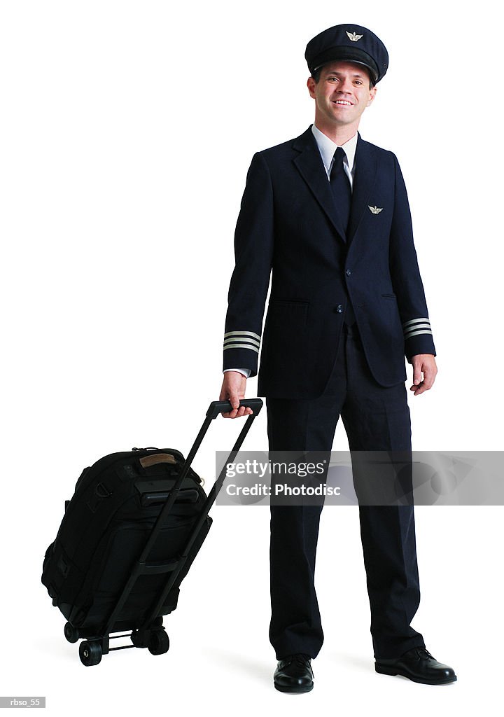 A caucasian male airline pilot smiles as he pulls his luggage