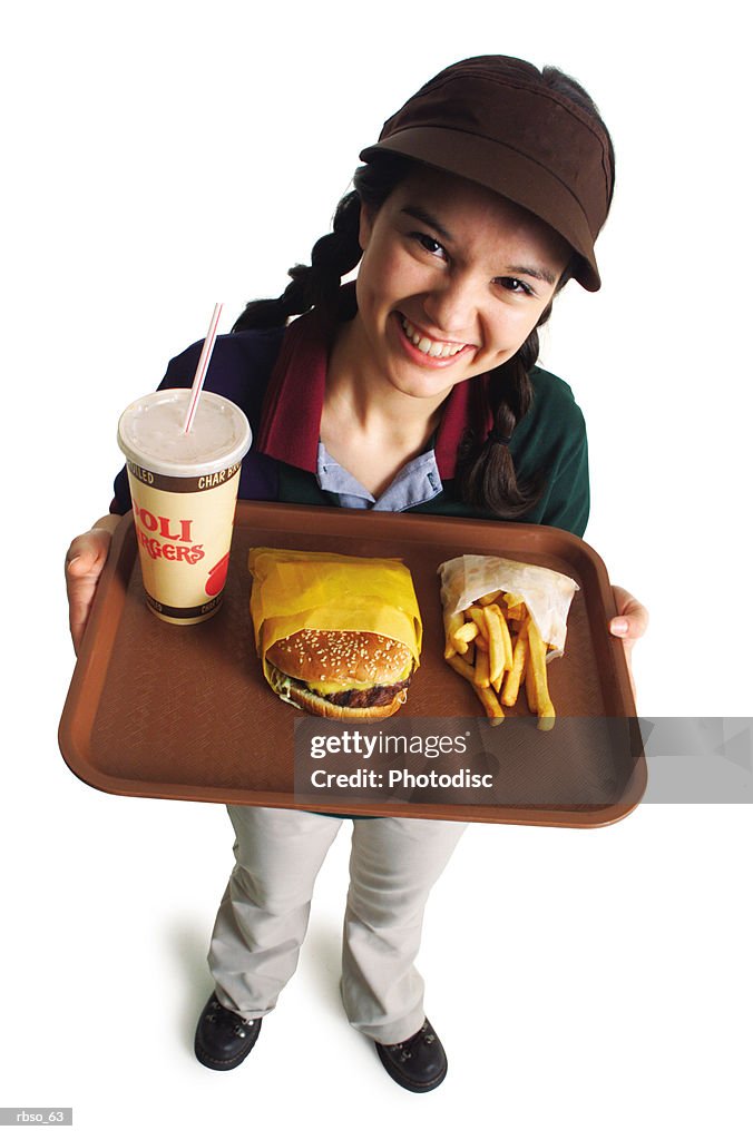 A teenage caucasian girl in a fast food uniform serves a burger and fries as she smiles and looks up at the camera